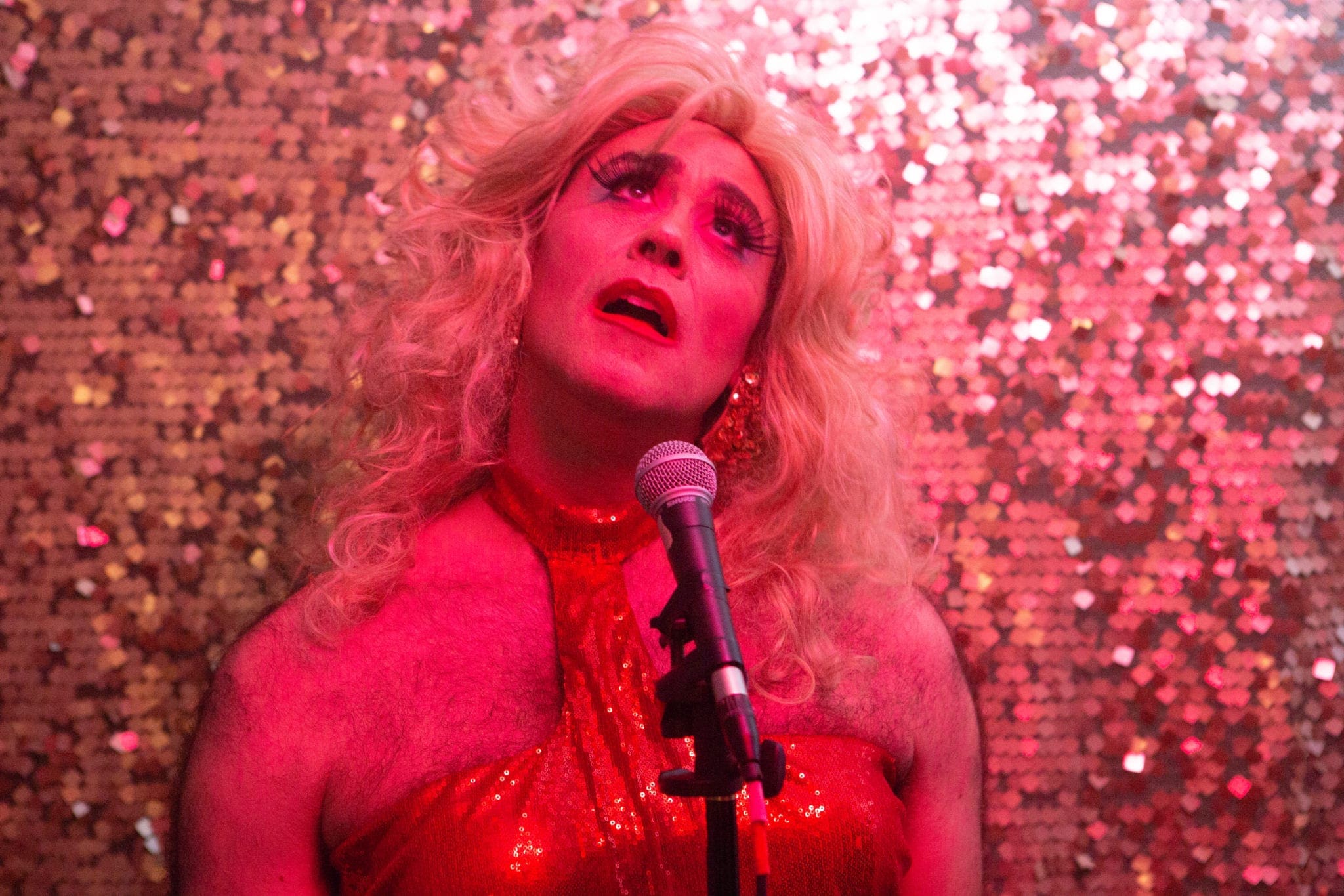 Martha Graham Cracker in a red dress dress against a red sparkly background singing into a mic with a mournful expression